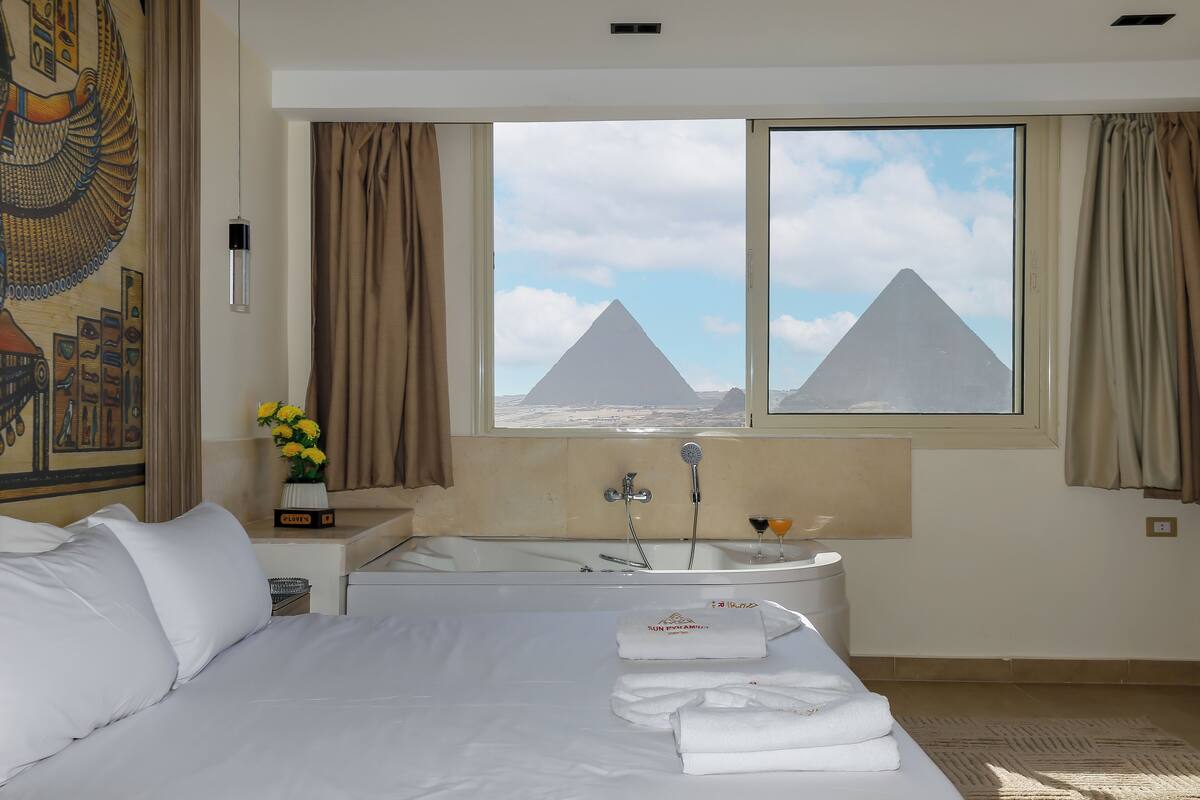 Habitación de hotel con cama, bañera y ventana con vistas a pirámides.