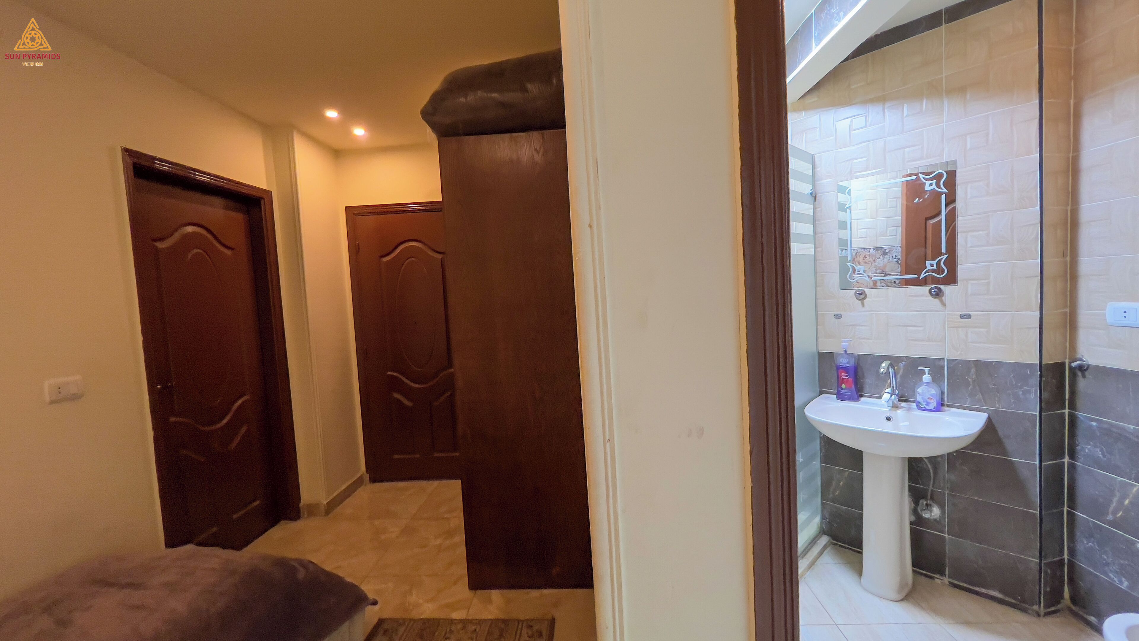 Un pasillo con dos puertas de madera, un lavabo blanco con espejo y una pared de azulejos.
