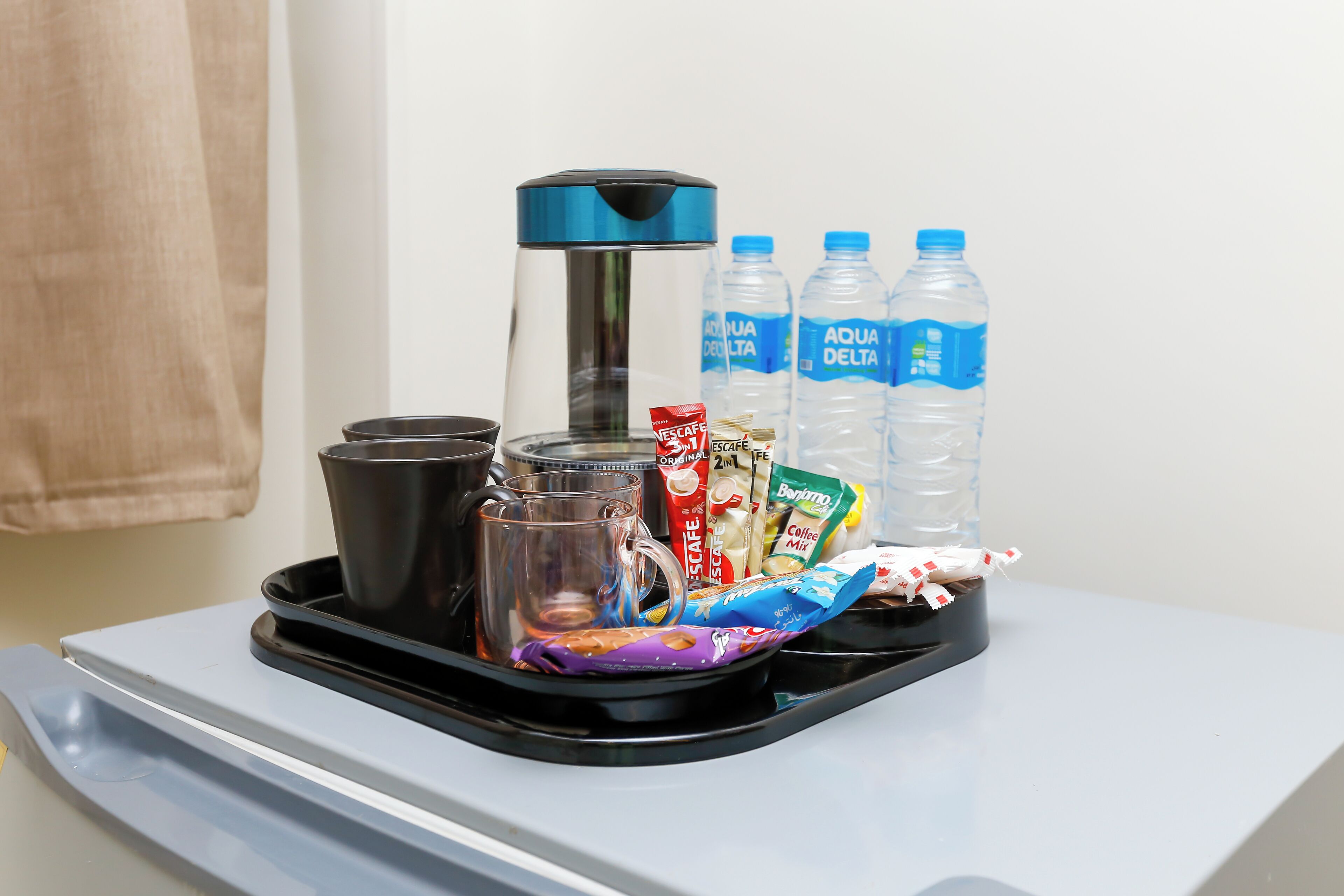 A tray with a coffee maker, cups, water bottles, and coffee packets on a table.