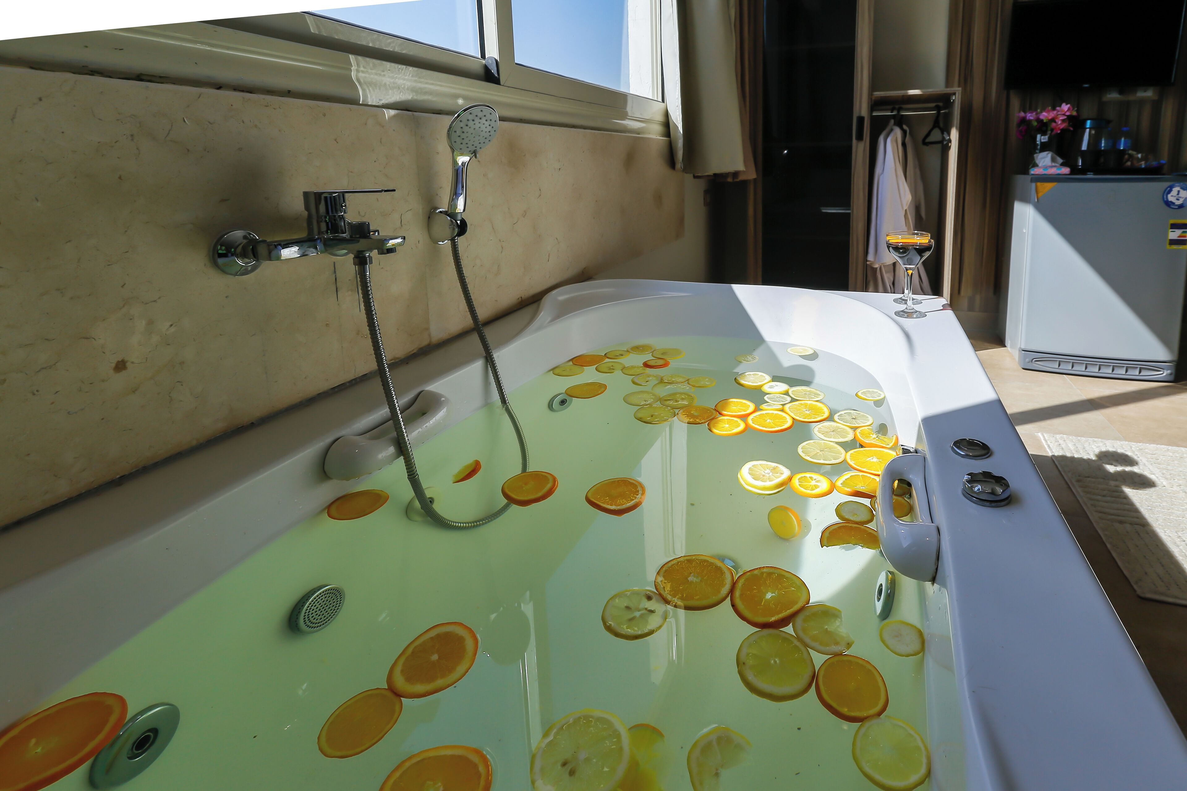 A bathtub filled with water and orange slices, a showerhead, and a towel rack in the background.