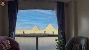 A room with a view of the pyramids, a purple armchair, a grey armchair, and a potted plant. - Sun Pyramids View Inn (Giza)