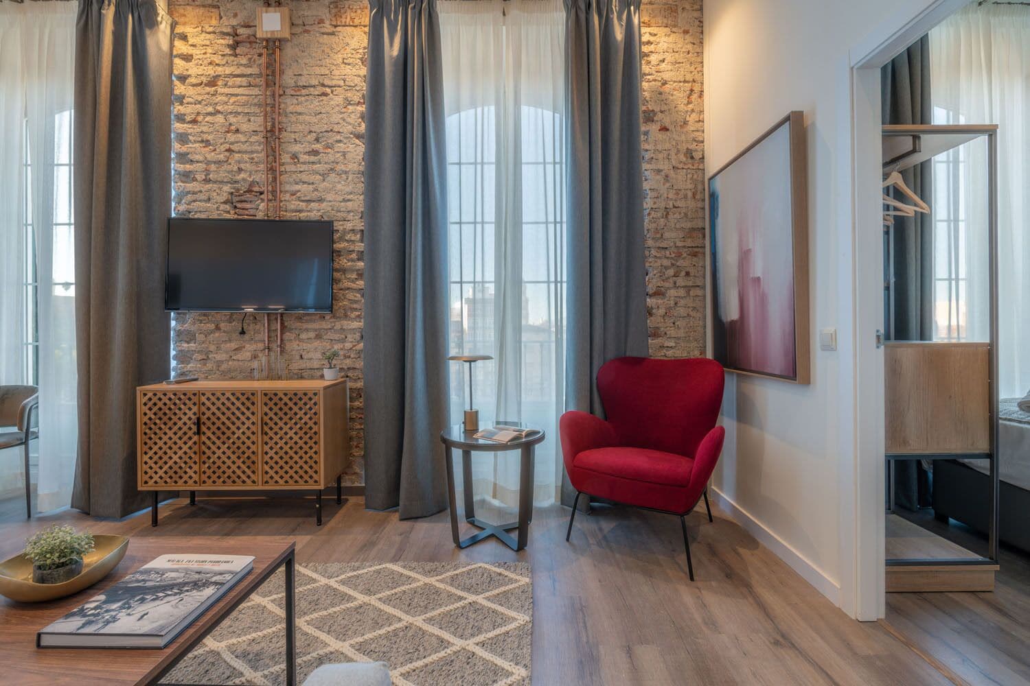 A modern living room with a stone wall, a red armchair, a TV, and a wooden cabinet.