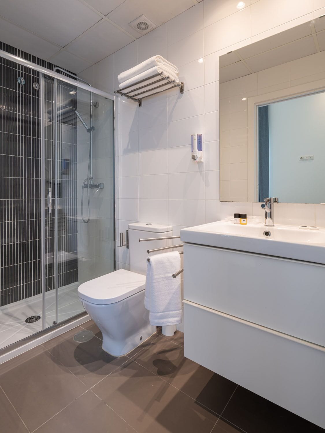 A modern bathroom with a glass-enclosed shower, a toilet, and a vanity with a mirror.