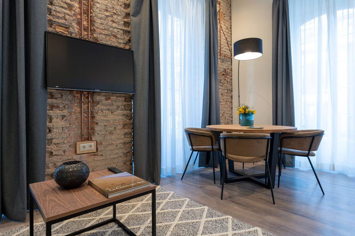 A modern dining area with a brick wall, a flat-screen TV mounted above a table, and a pendant light.