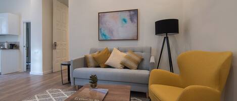 A modern living room with a sofa, a yellow armchair, a coffee table with a book, a floor lamp, and a painting on the wall.