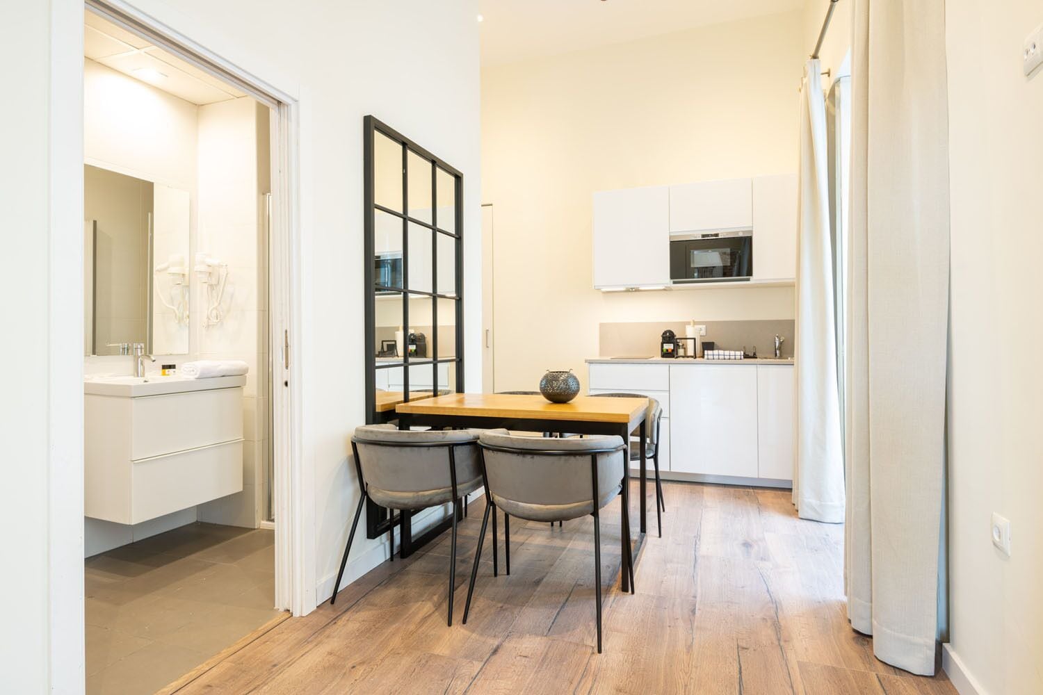 A compact kitchen with a dining area, white cabinets, a microwave, and a wooden table with two chairs.