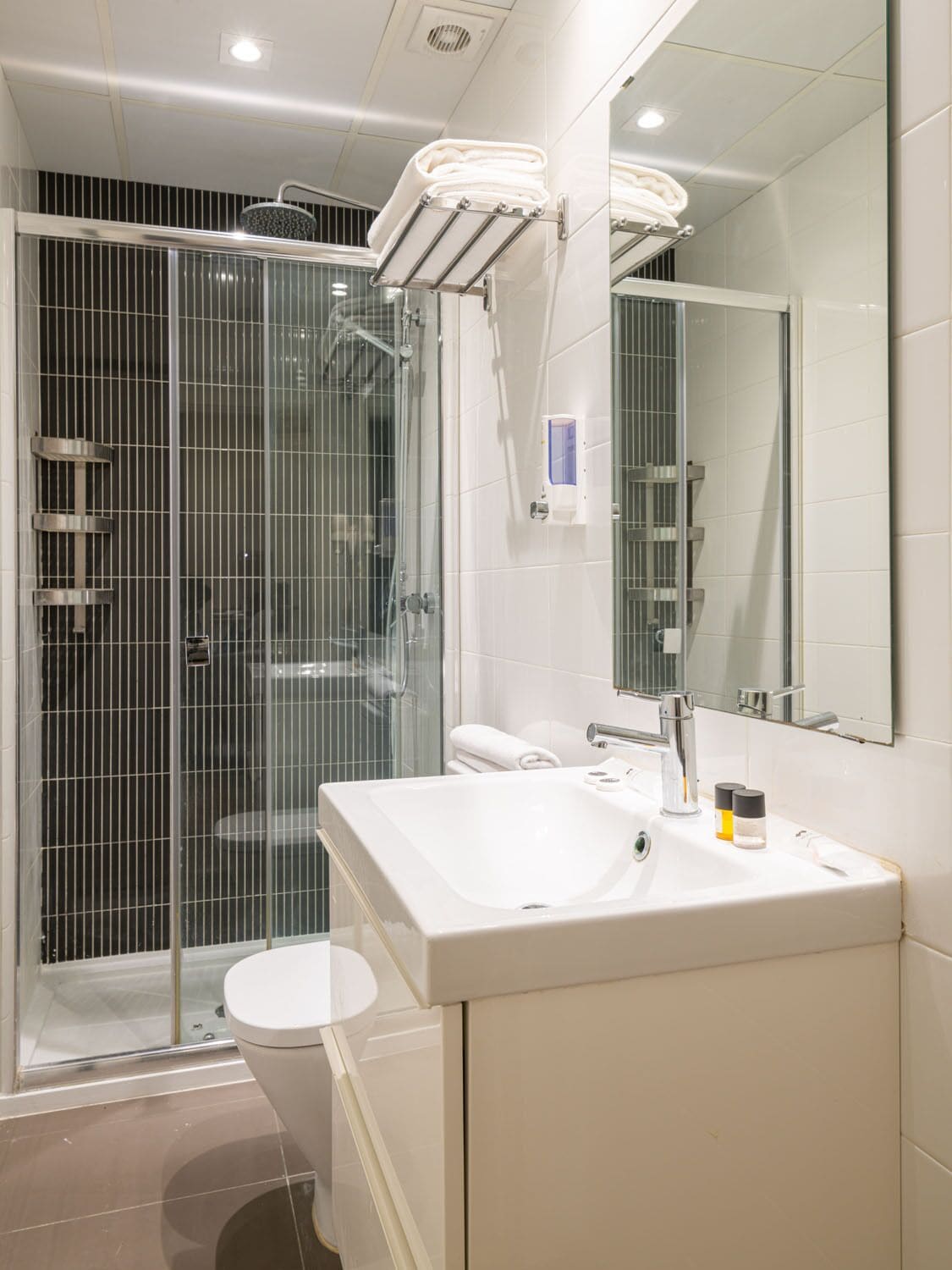 A modern bathroom with a glass-enclosed shower, a white sink, and a large mirror.