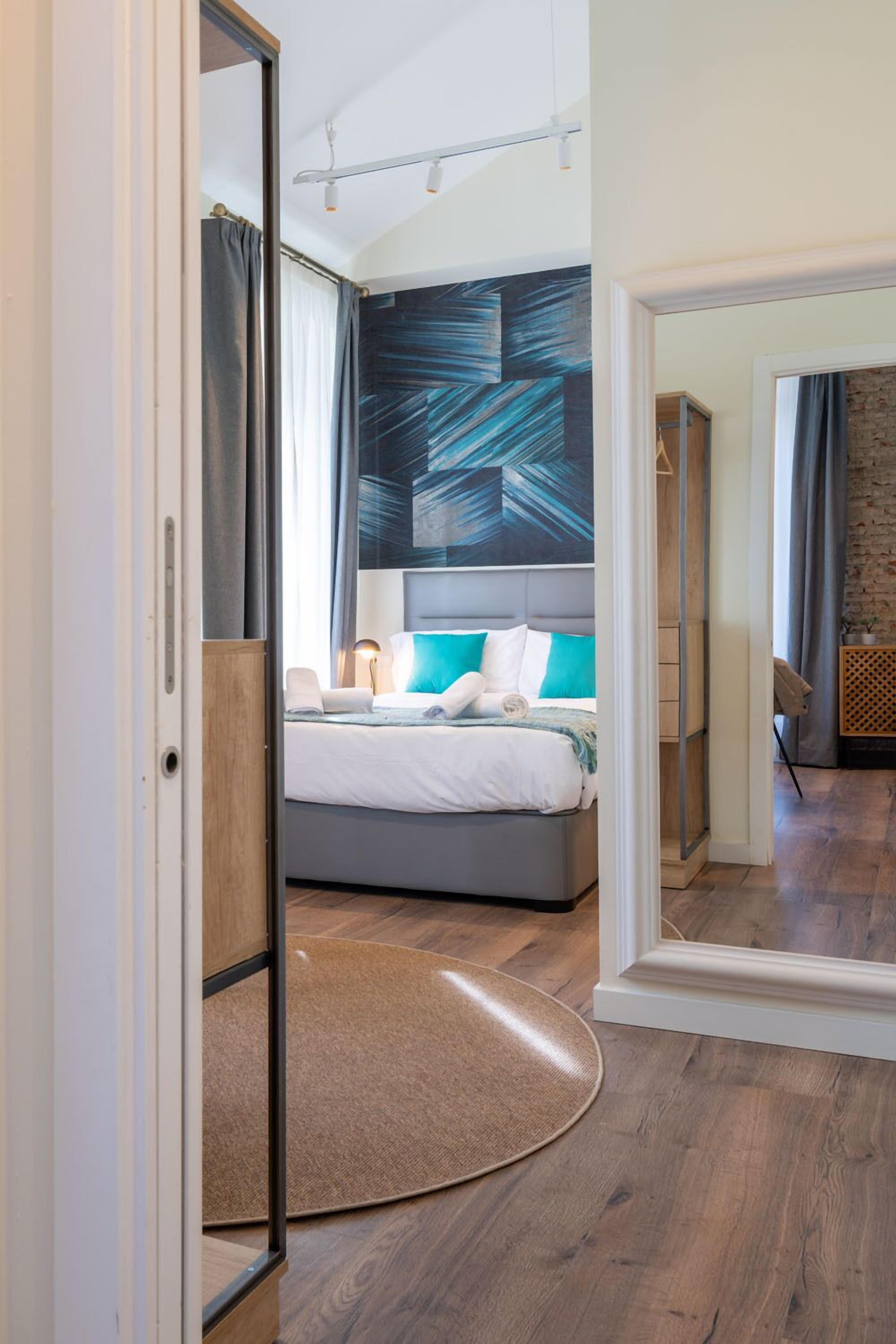 A modern hotel room with a large bed, a mirror, and a view of the hallway.