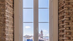 A room with a large window featuring a view of a cityscape, including a prominent building with a clock tower. - Homeart Apartments Malaga (Málaga)