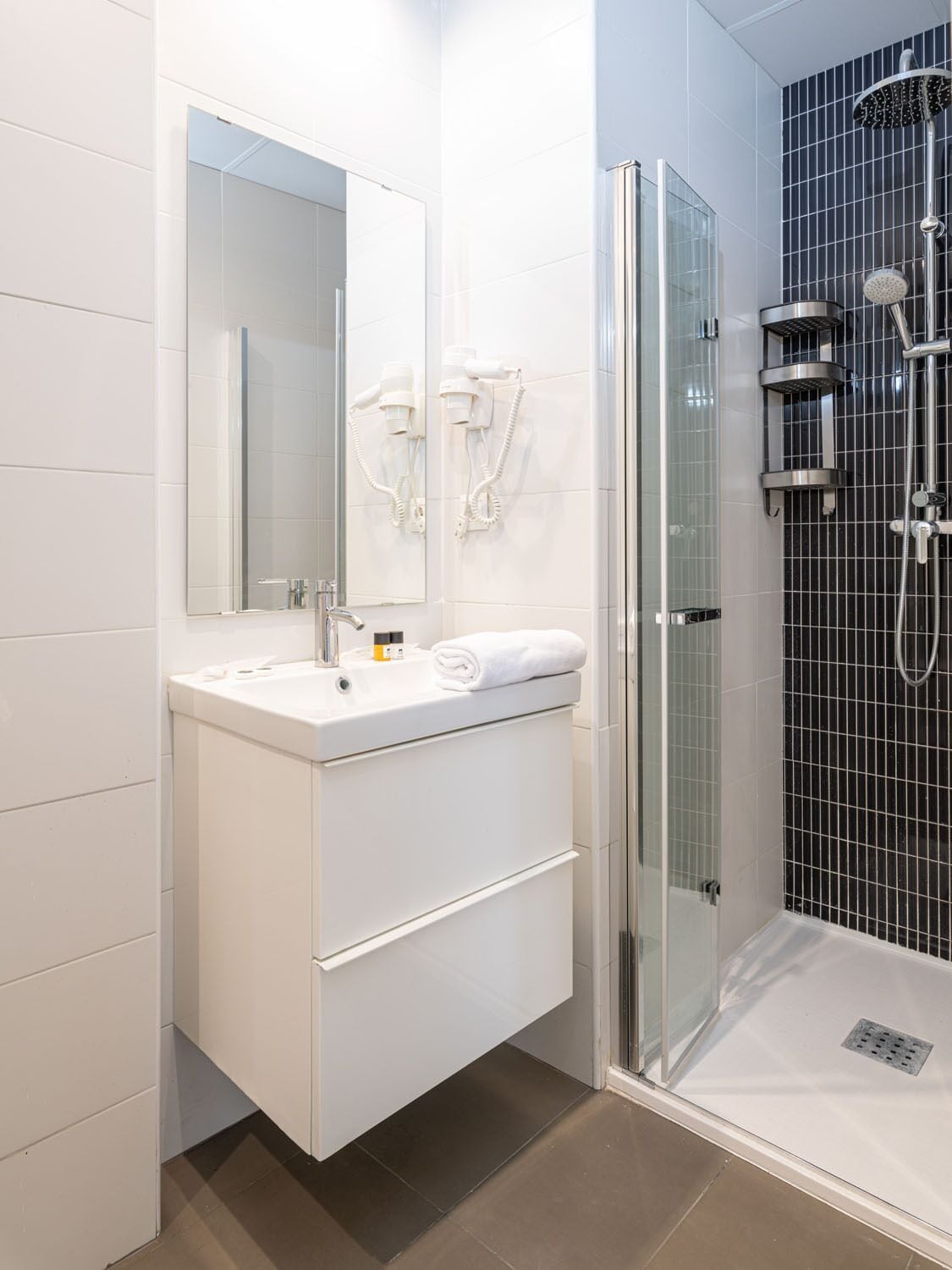A modern bathroom with a glass shower enclosure, a white vanity with a mirror, and a towel on the counter.