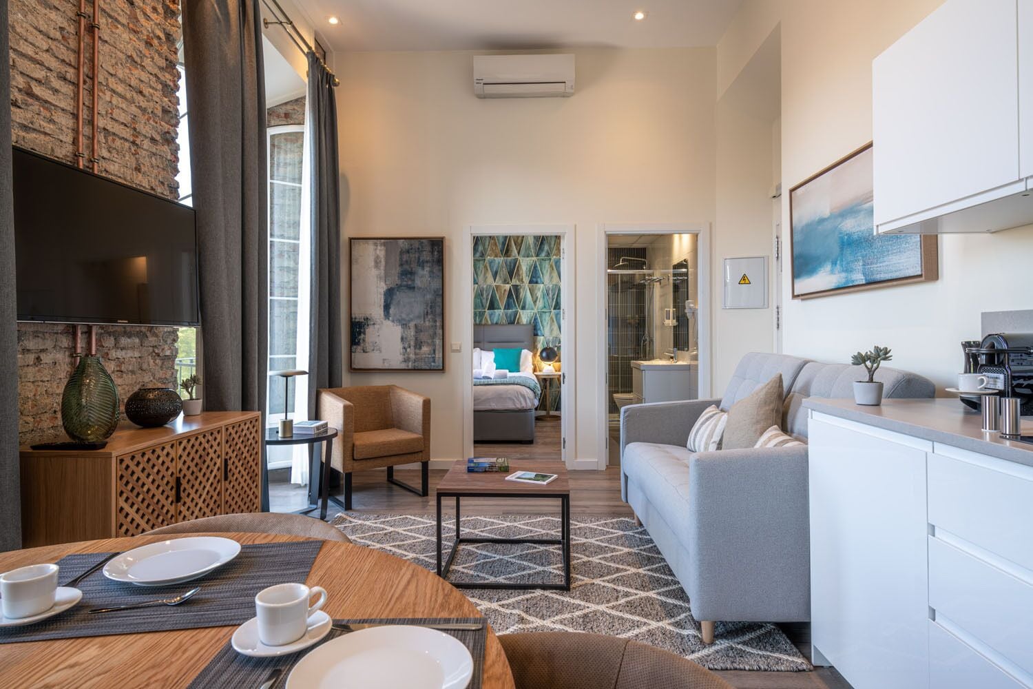 A modern hotel room with a kitchen, a dining area, and a living space.