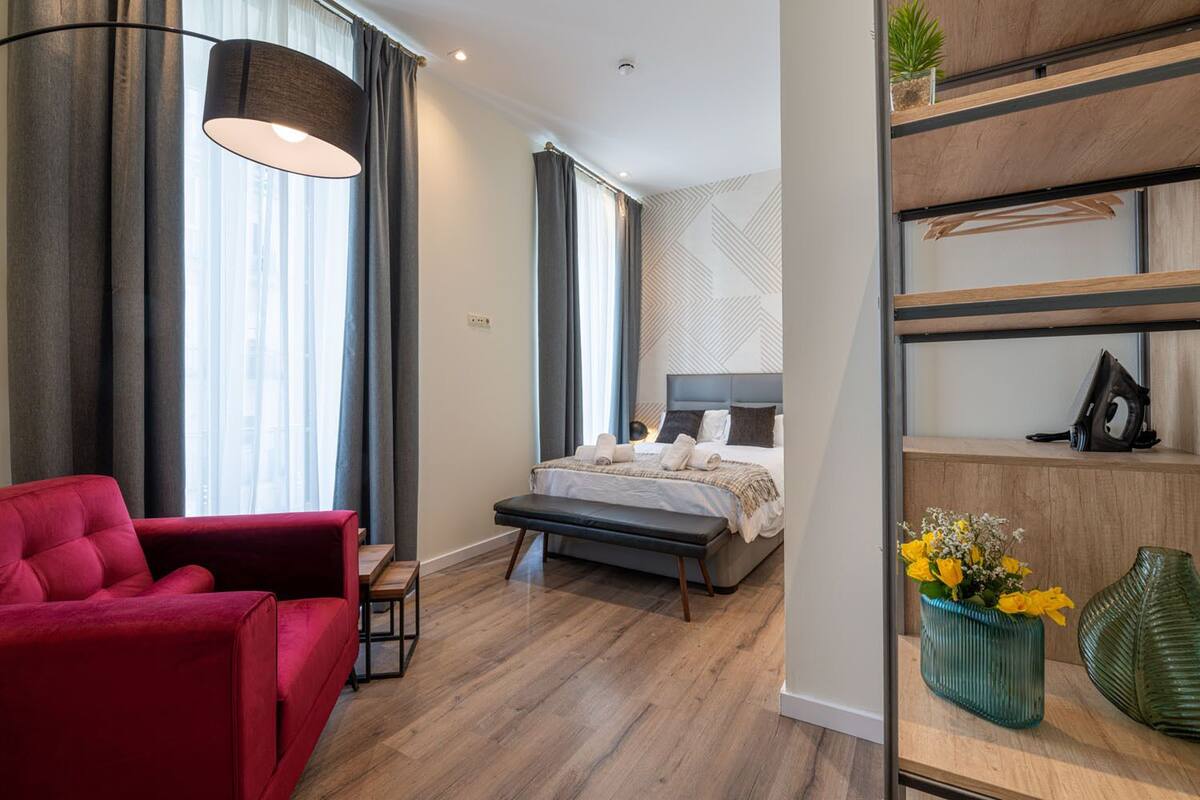 A modern bedroom with a bed, a red armchair, a bench, and a shelf with decorative items.