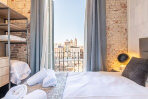 A hotel room with a bed, a wooden wardrobe, a window with curtains, and a view of buildings. - Homeart Apartments Malaga (Málaga)
