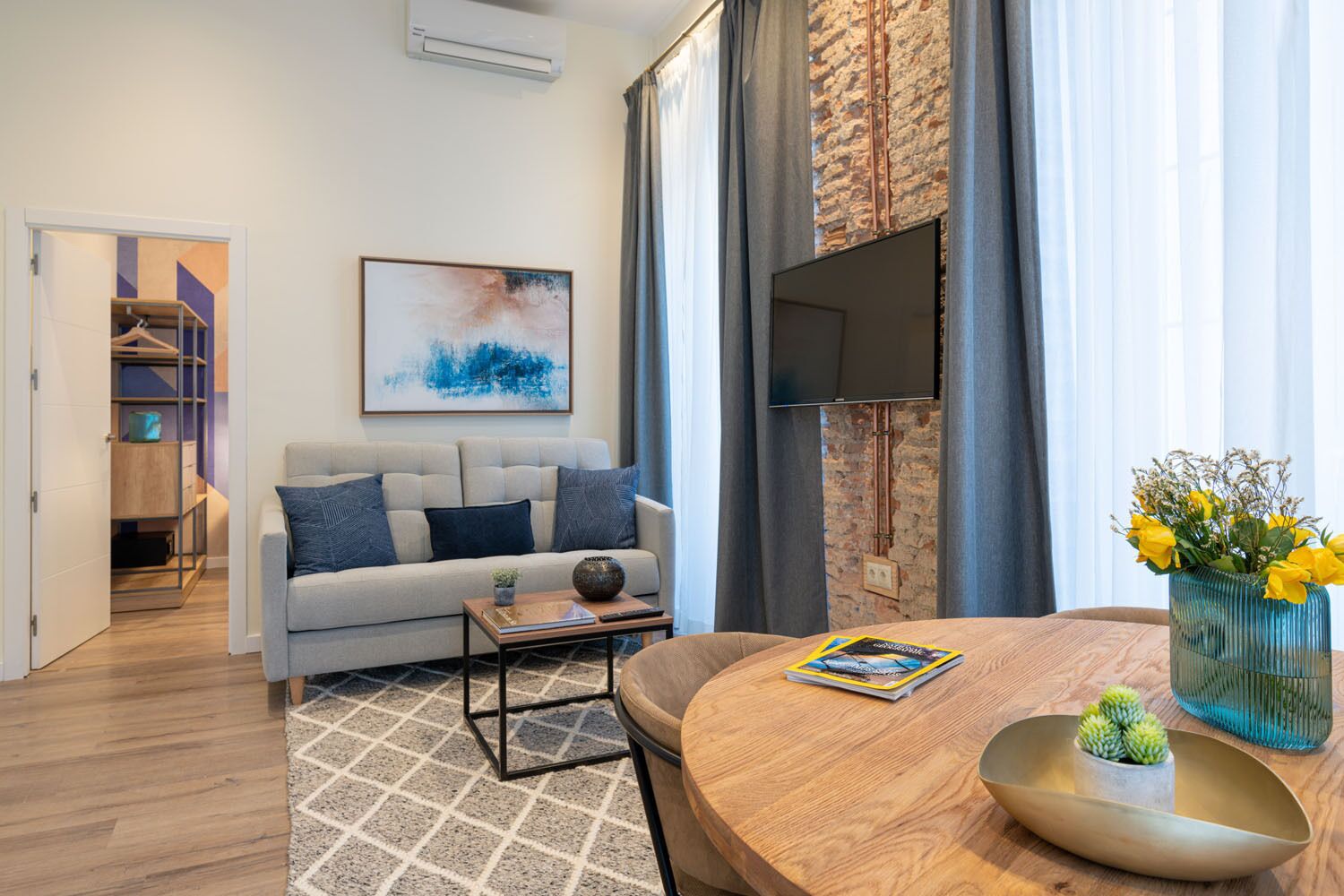 A modern living room with a sofa, coffee table, and a dining table with a vase of flowers.