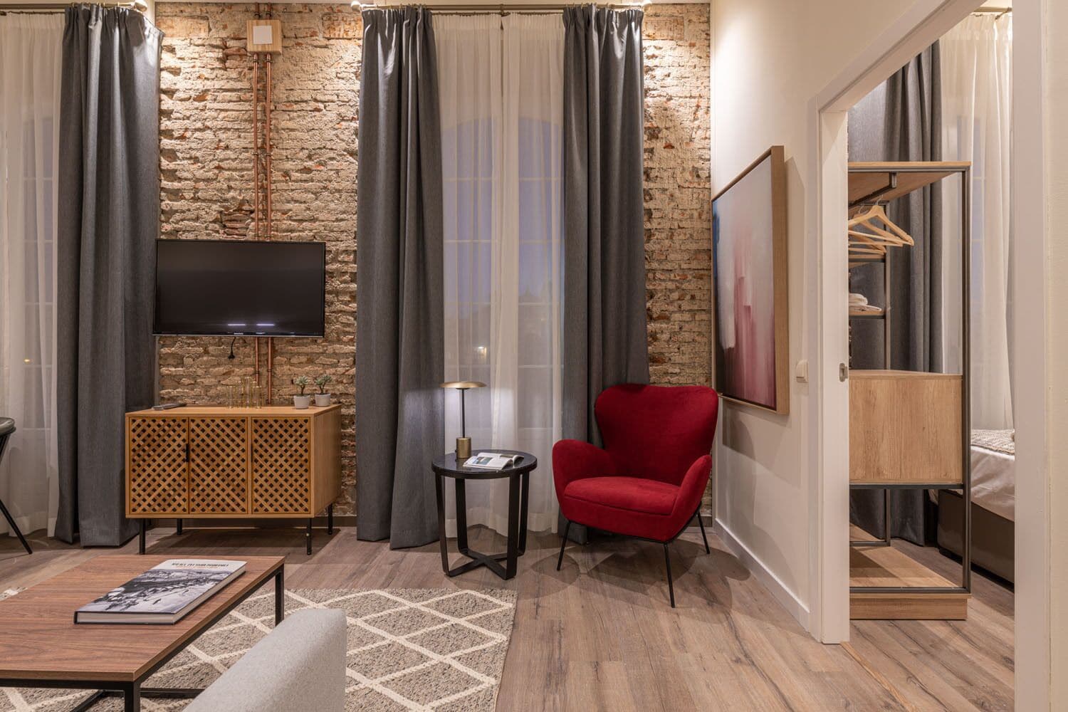 A modern living room with a stone wall, a flat-screen TV, a red armchair, a small side table, and a wooden cabinet.