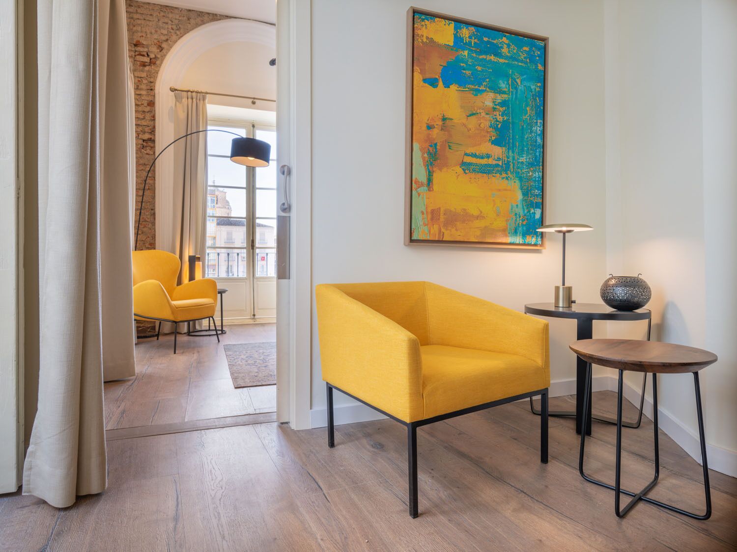 Een moderne woonkamer met een gele fauteuil, een ronde houten tafel en een groot abstract schilderij aan de muur.