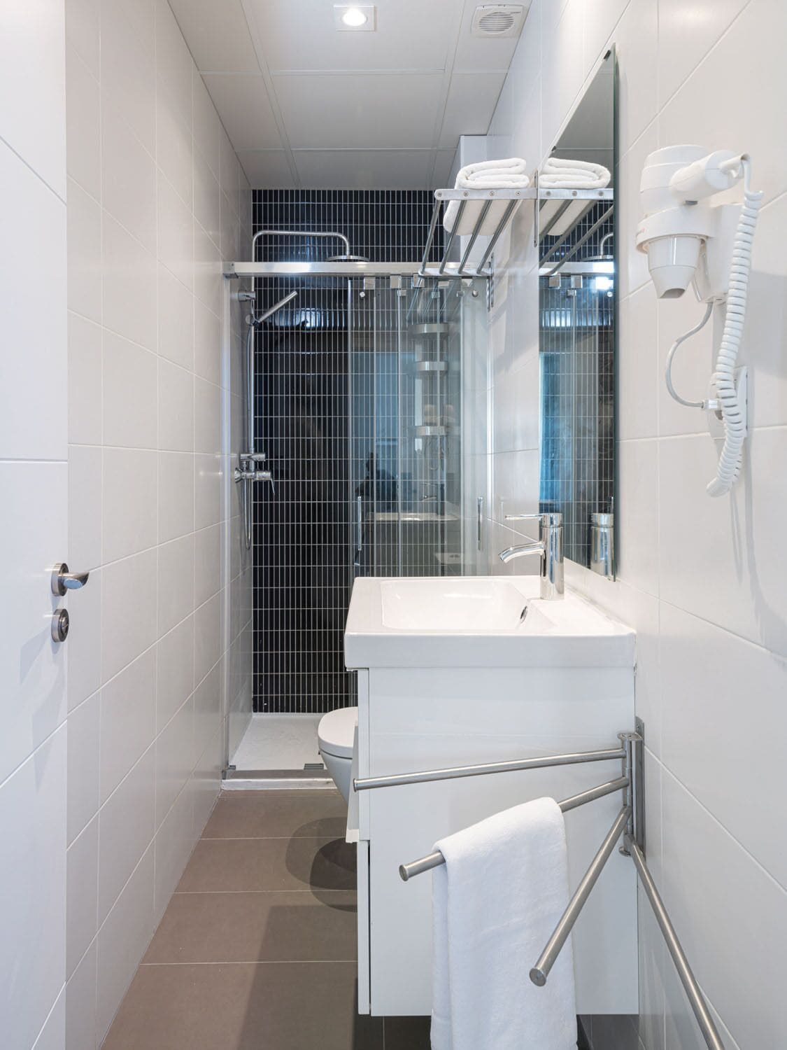 A modern bathroom with a glass shower enclosure, a white sink, and a towel rack.