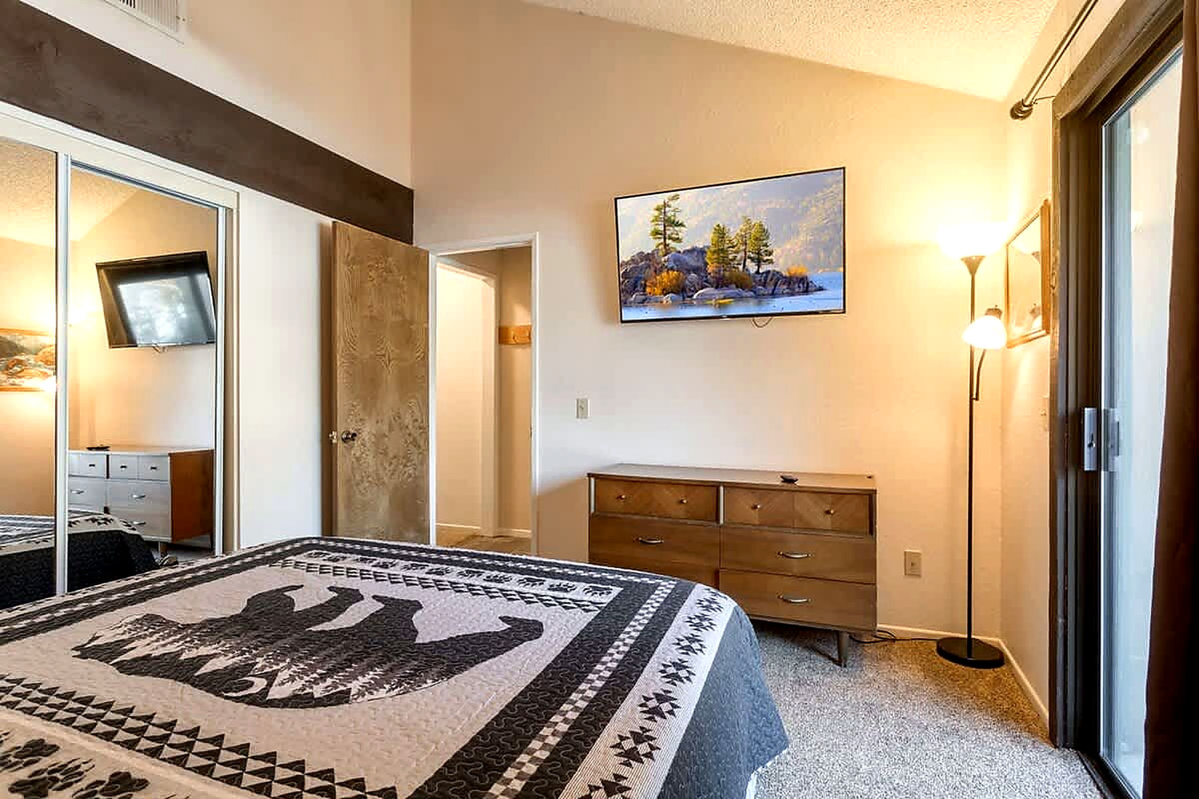 A bedroom with a bed, a dresser, a painting, and a lamp.