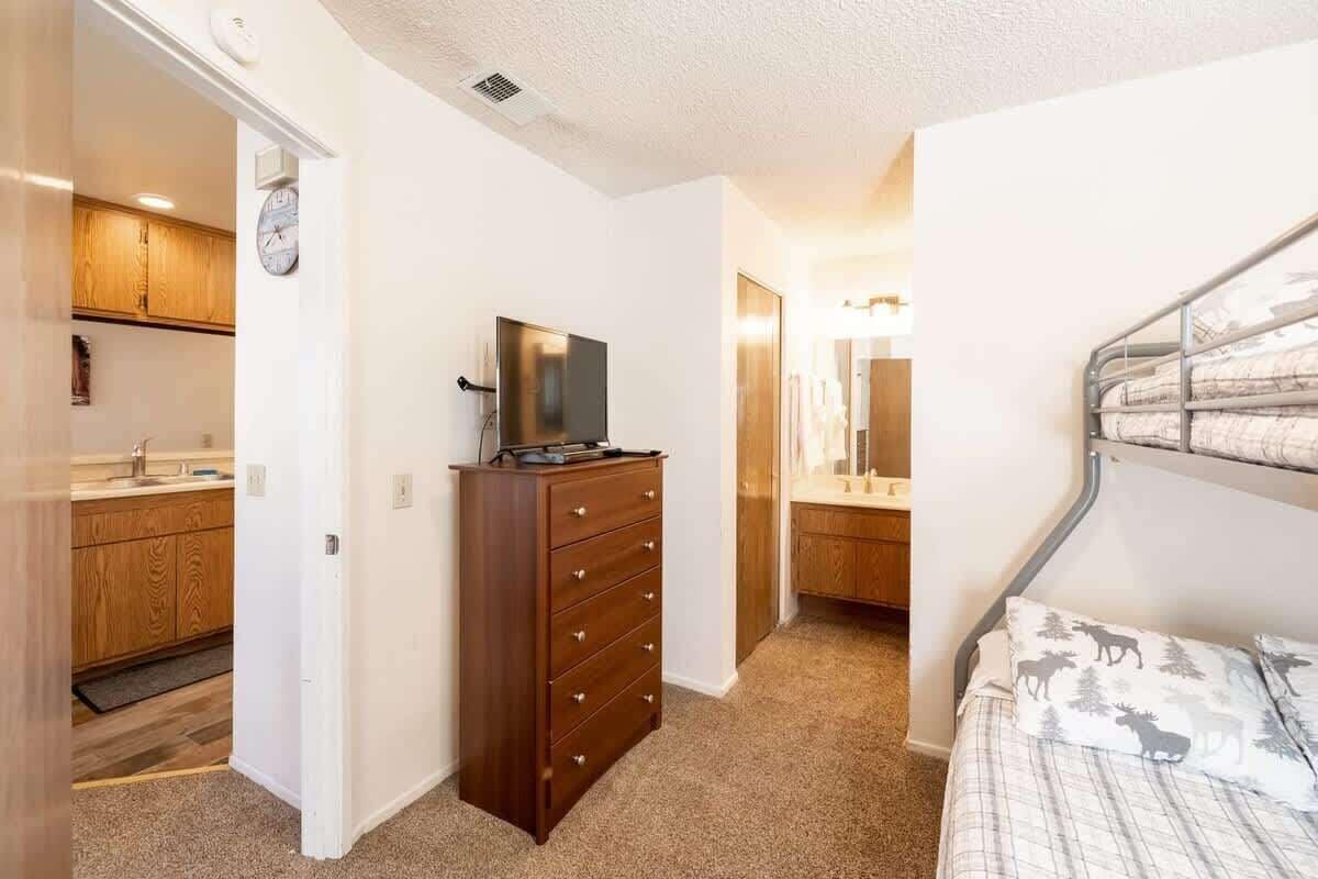 A bedroom with a bed, a dresser, a television, and a bathroom with a mirror.