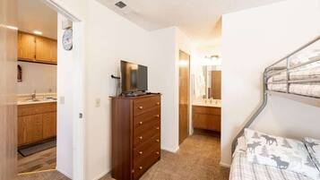 A bedroom with a bed, a dresser, a television, and a bathroom with a mirror.