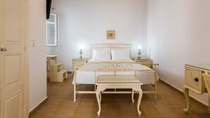 A bedroom with a bed, bedside tables, a nightstand, a bench, and a door. - In the historical center of Adamas (Milos)