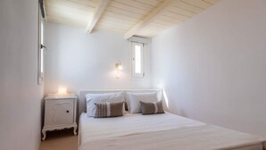 A bedroom with a bed, nightstand, and a window. - In the historical center of Adamas (Milos)
