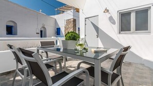 A white building with a balcony, a table with chairs, a potted plant, and a window. - In the historical center of Adamas (Milos)