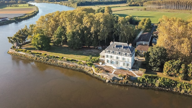 Vue aérienne d’un vaste domaine traversé par une rivière, entouré d’une végétation luxuriante et de champs.