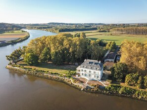 Een luchtbeeld van een groot landgoed met een rivier, omringd door weelderige begroeiing en velden.