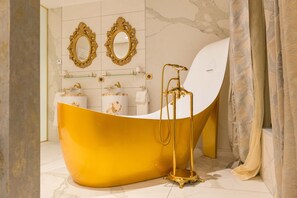 Une salle de bain avec une baignoire dorée, deux miroirs richement décorés et un lavabo blanc.