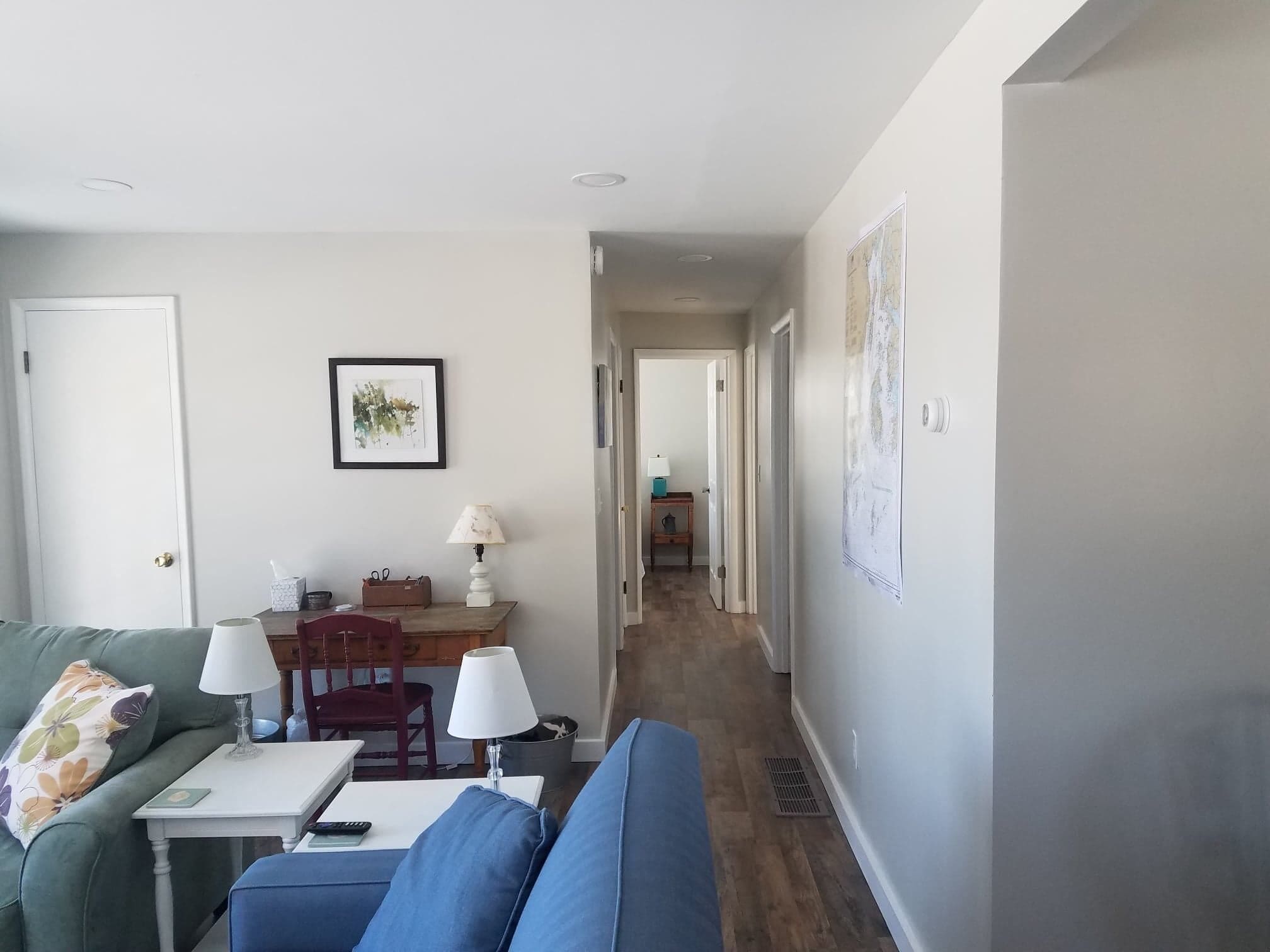 Un salon avec un canapé vert, un canapé bleu, une petite table avec une lampe et un tableau encadré au mur.