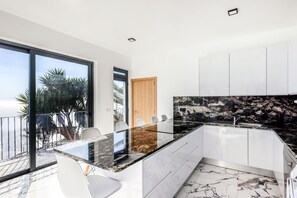 Une cuisine moderne avec un îlot central en verre, des armoires blanches et une vue sur les palmiers.
