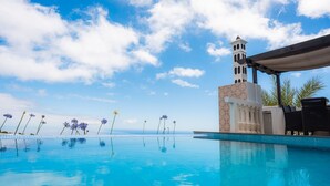 Une piscine avec une eau d’un bleu limpide, un bâtiment blanc surmonté d’une tour et un ciel dégagé.
