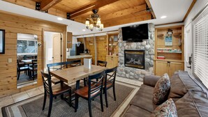 L’intérieur chaleureux d’un chalet avec un coin repas en bois, une cheminée en pierre et un espace salon confortable.