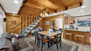 Un vaste espace de vie comprenant un escalier en bois, une table à manger avec des chaises et un coin cuisine avec un bar.