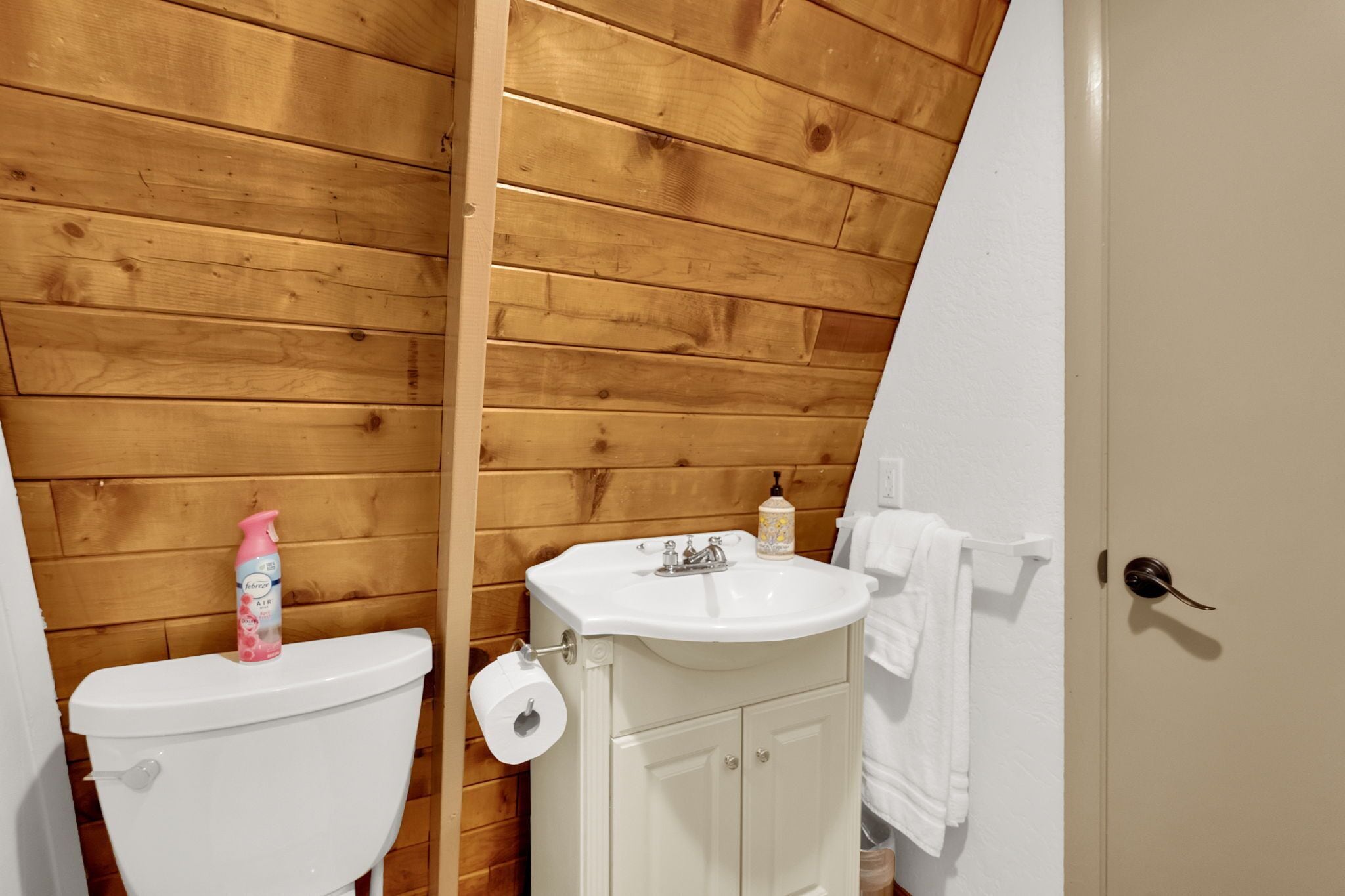 A bathroom with a wooden ceiling, a white toilet, a sink, and a towel hanging on the wall.