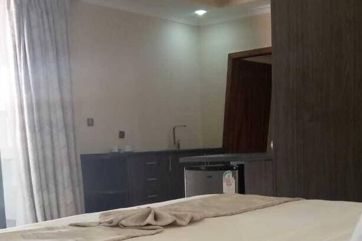 A hotel room with a bed, a small kitchenette, and a bathroom.