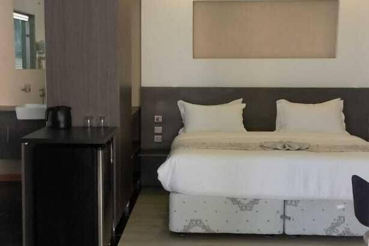 A hotel room with a bed, bedside table, and a small kitchenette area.