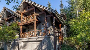 A multi-story wooden house with a balcony, garage, and surrounded by trees.