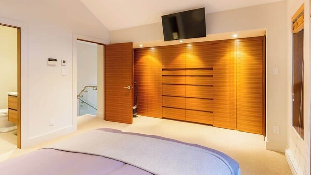 A bedroom with a bed, wooden wardrobe, a television, and a bathroom.