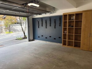 Un garaje con piso de concreto, una pared azul con múltiples ganchos y un gabinete de madera con estantes.