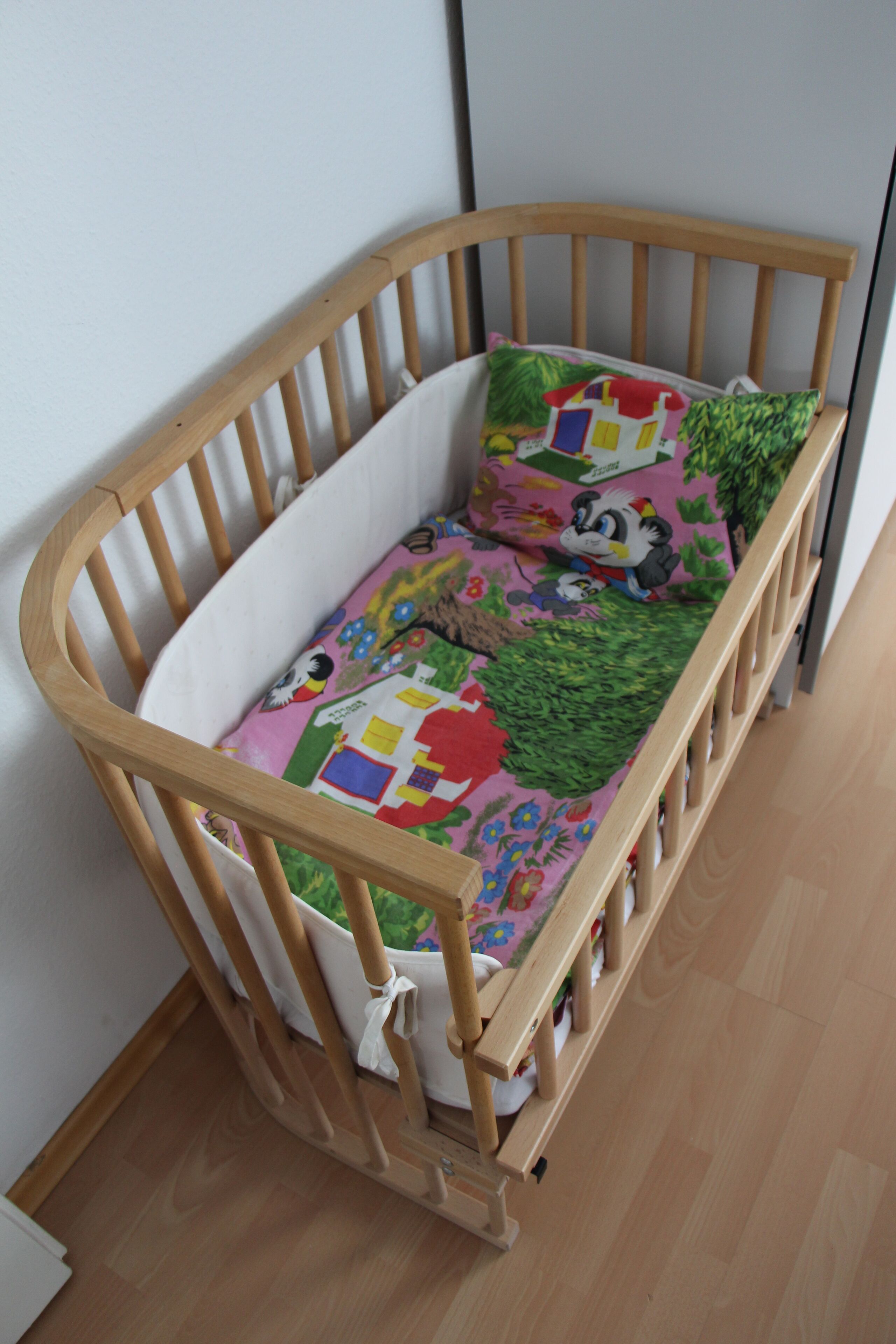 A wooden crib with a colorful quilted mattress and a green pillow.