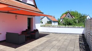 Een terras met tuinmeubilair, een rood zonnescherm en uitzicht op omliggende huizen.