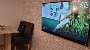 Een moderne kamer met een flatscreen televisie waarop een advertentie voor een accommodatie wordt getoond, een houten tafel en zwarte leren stoelen.