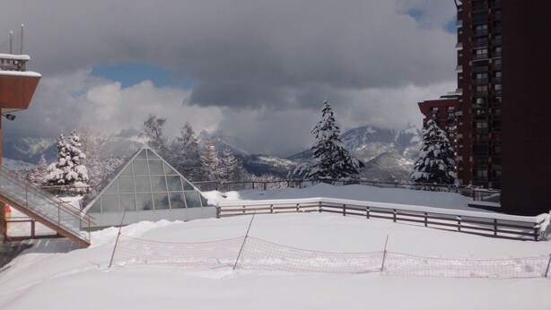 A snow-covered outdoor area with a glass-roofed structure, a wooden fence, and snow-laden trees. - Studio at the foot of the slopes, for 2 people. (Villarembert)