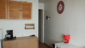 A room with a wooden cabinet, a white table with a red lamp, and a clock on the wall. - Studio at the foot of the slopes, for 2 people. (Villarembert)