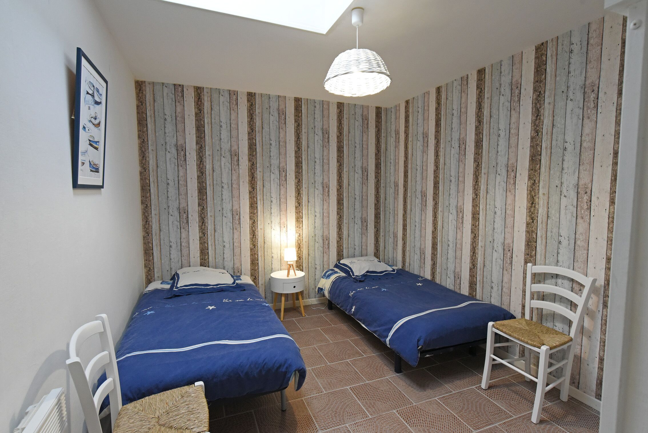 A bedroom with two beds, a small table, a chair, and a wall-mounted lamp.