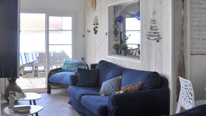 Un salon avec un canapé bleu, une petite table et un fauteuil. Il y a une fenêtre donnant sur l’extérieur.