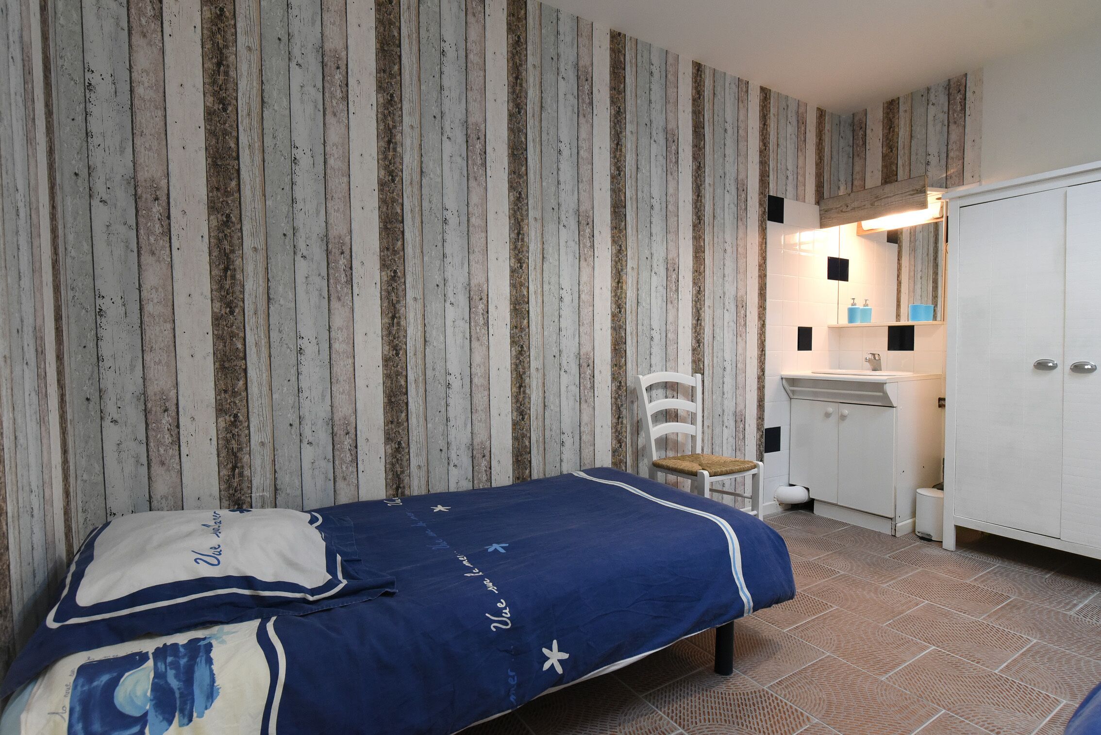 Une chambre à coucher comprenant un lit, une chaise, une petite armoire blanche et un panneau mural en bois.