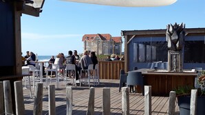 Un espace extérieur aménagé avec des tables et des chaises en bois, offrant une vue sur l’océan.